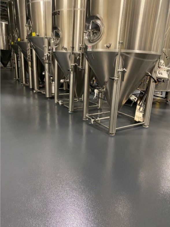 Stainless steel brewing tanks in an industrial facility with a gray epoxy floor.