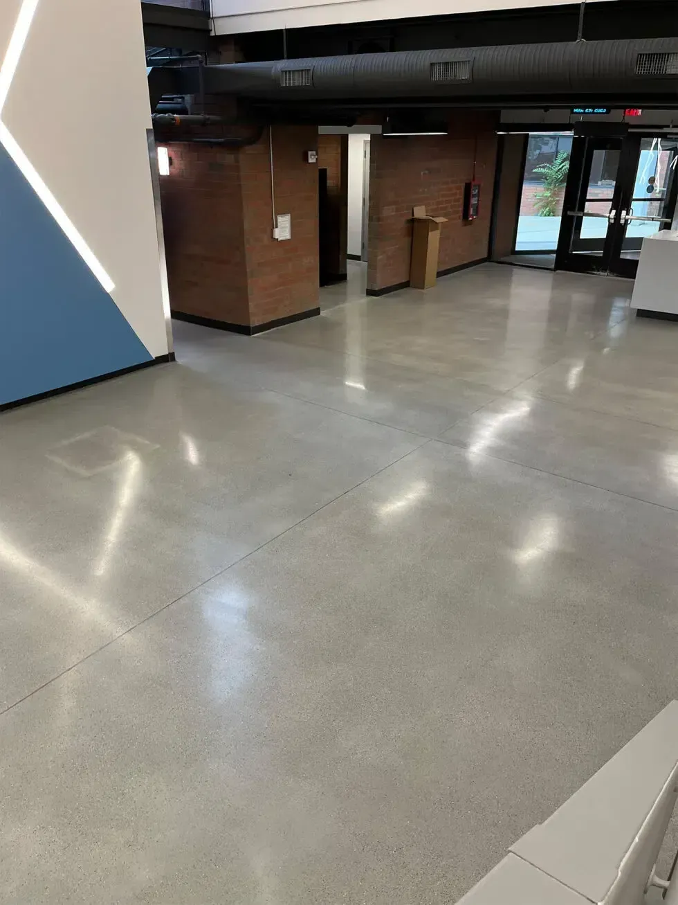 Empty indoor hallway with polished concrete floor, brick walls, and glass doors at the far end.