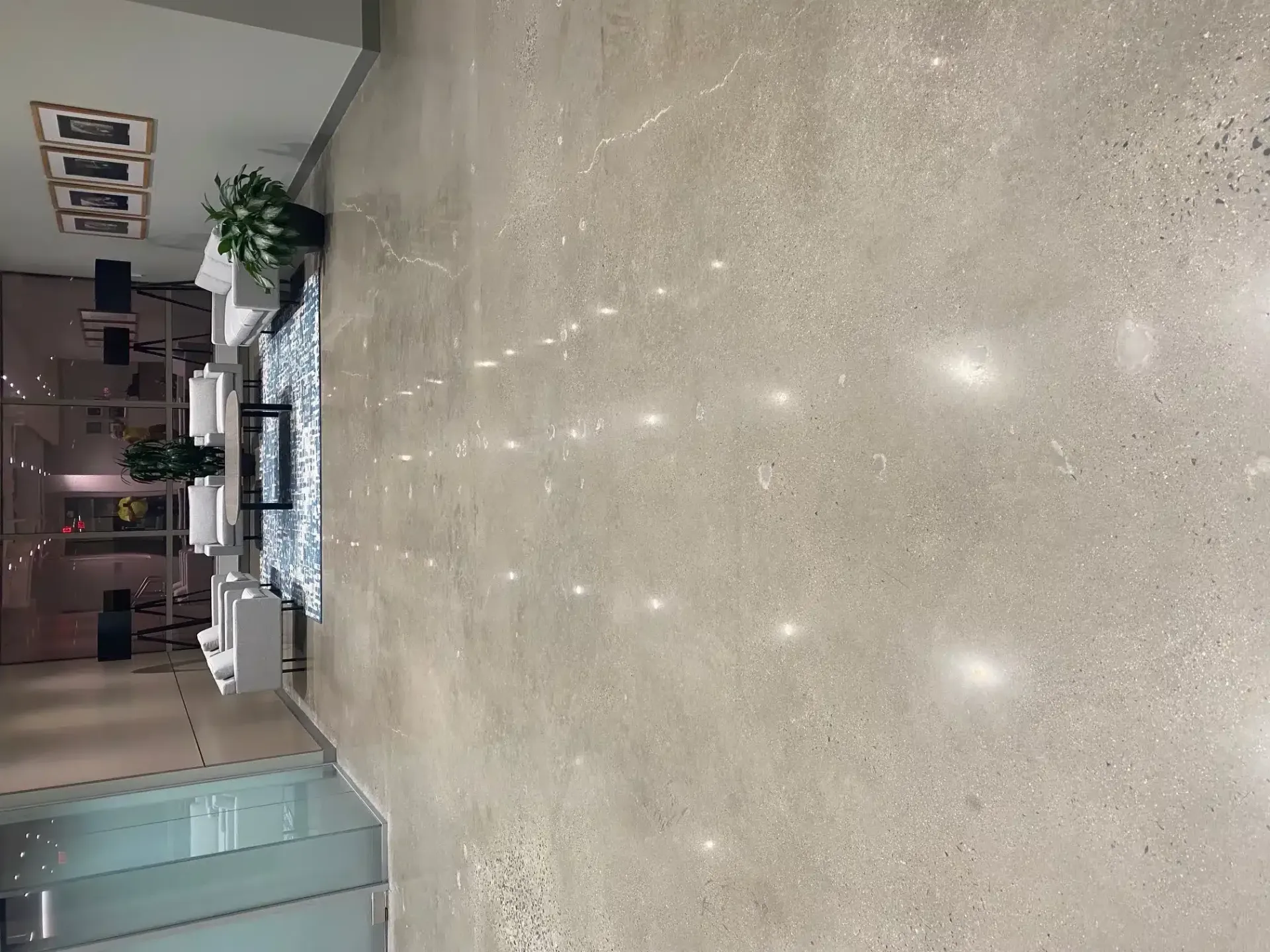 Modern lobby with polished floor, seating area, potted plants, and glass doors in the background