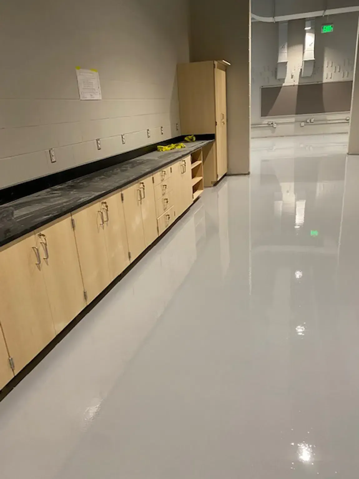 Empty lab counter with wood cabinets and glossy white floor in a hallway-like room.
