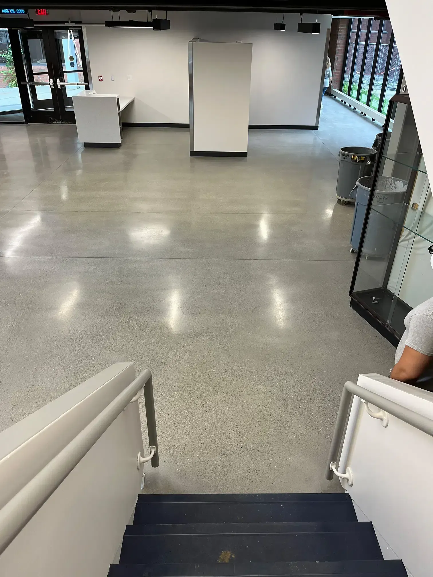 View from top of a staircase into a bright lobby with a polished floor and glass doors.