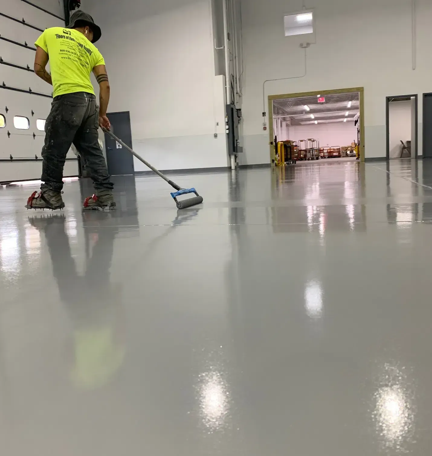 Worker in a neon shirt mopping a glossy gray floor in a large industrial room.