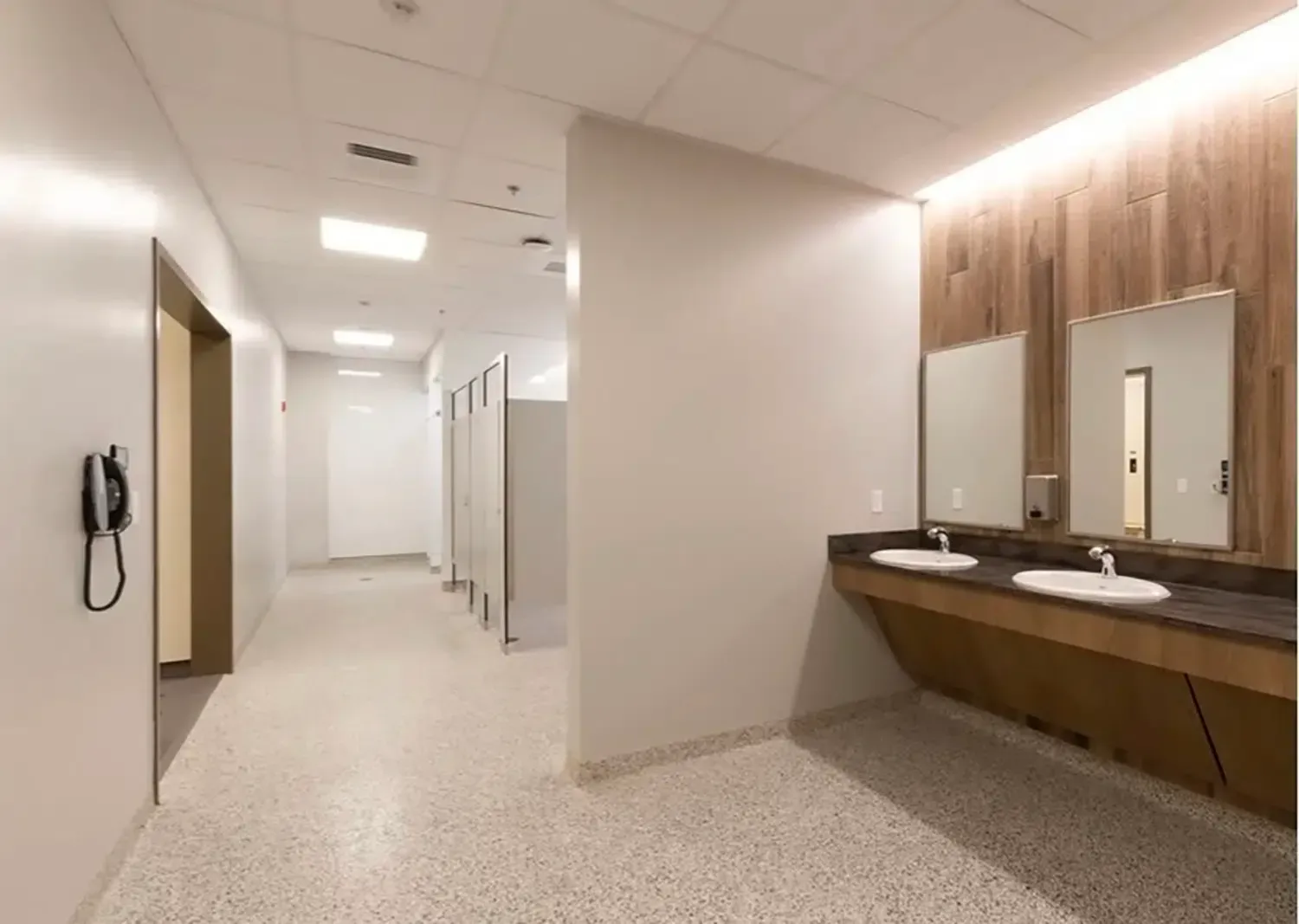 Modern restroom hallway with sinks, mirrors, and stalls under bright lighting