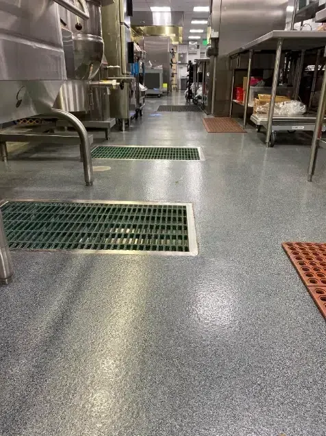 Industrial kitchen floor with stainless steel equipment and green grated drains