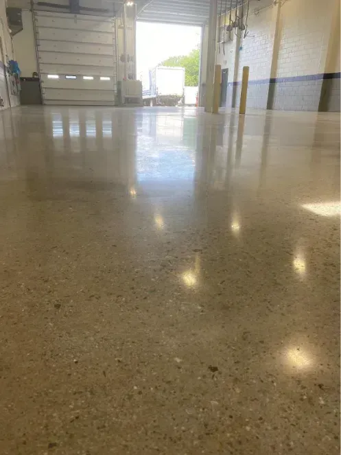 Polished concrete floor in an empty warehouse loading area with open garage door and daylight.