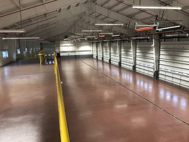 Empty industrial warehouse with rows of metal roll-up doors and a polished concrete floor.