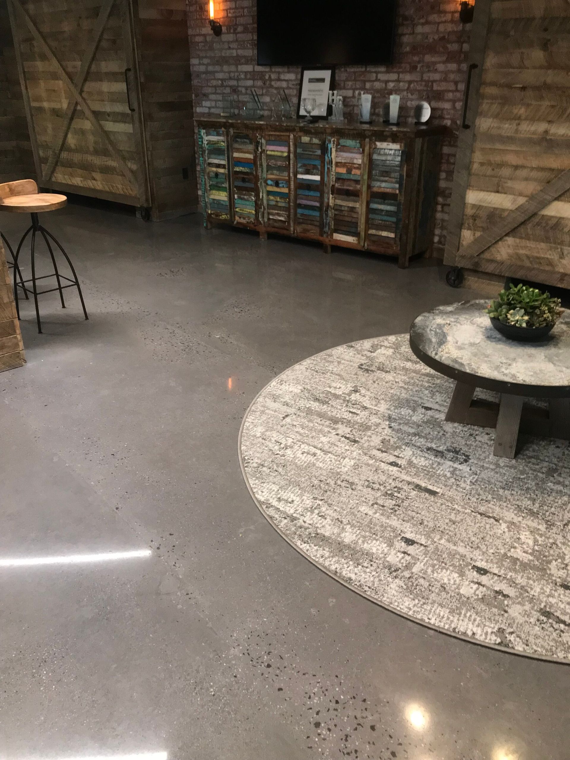 Rustic room with brick wall, wooden cabinets, gray floor, round rug, and small table with a plant.