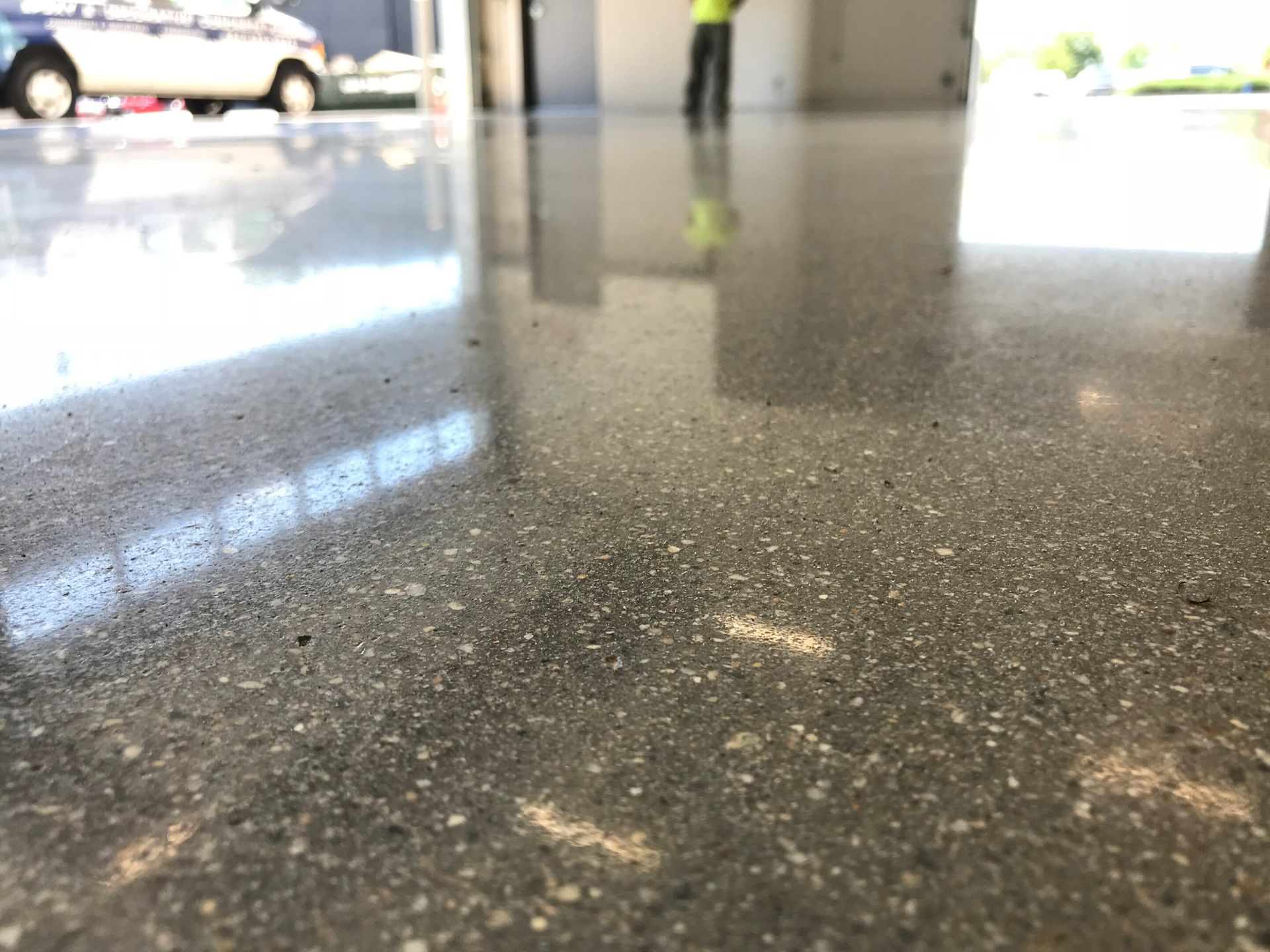 Shiny speckled floor reflecting a car and a person in a bright indoor space