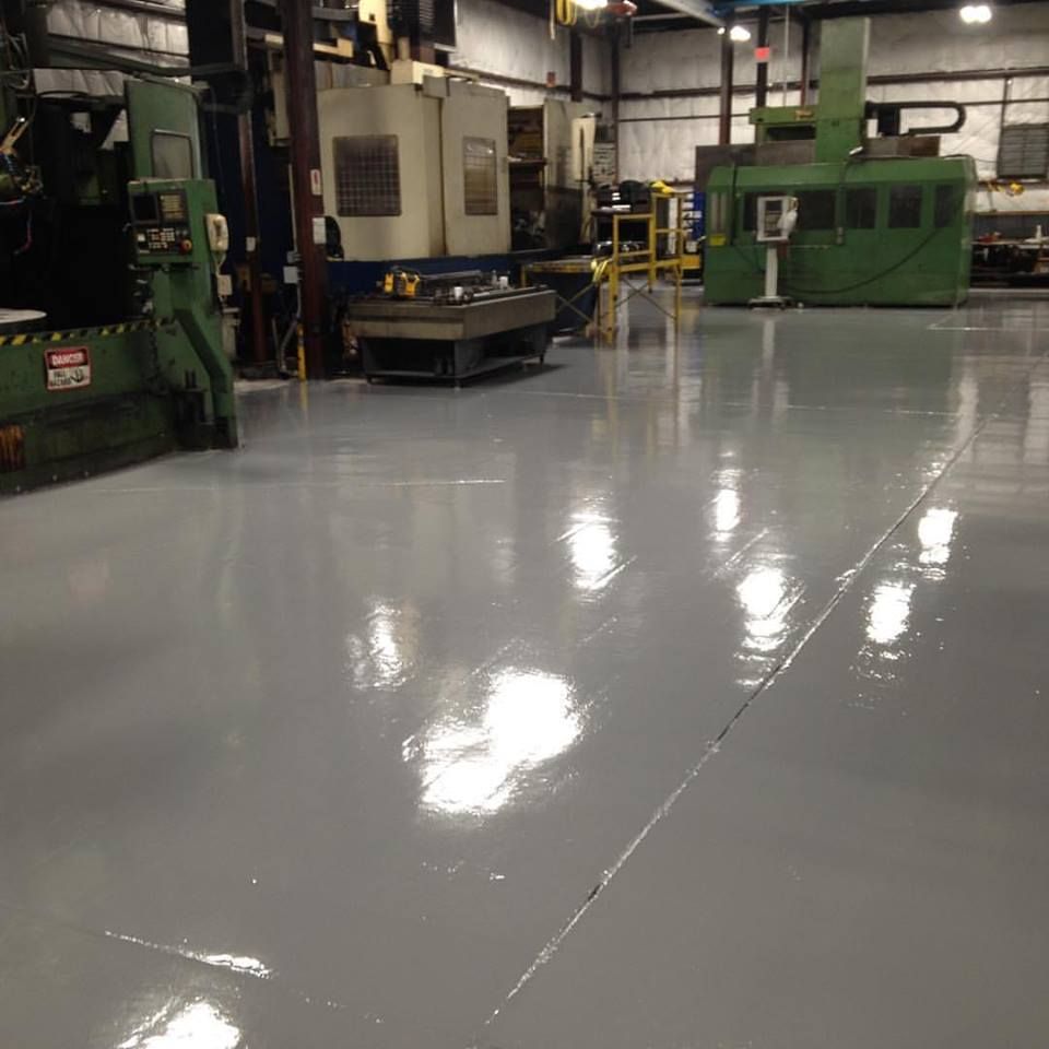 Industrial factory floor with large green machines and a glossy gray epoxy floor.