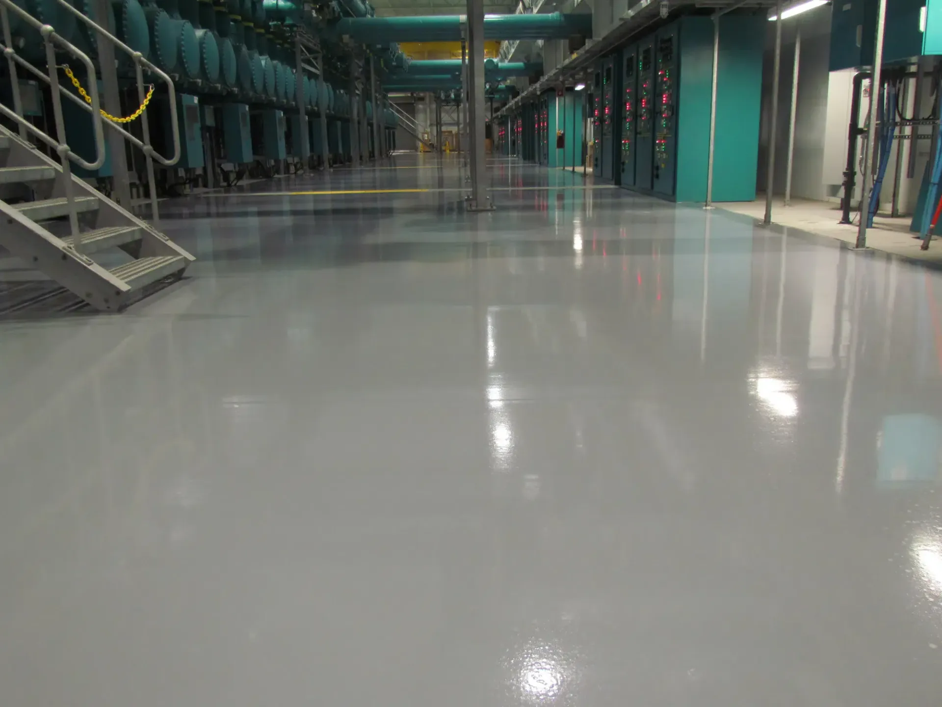 Empty industrial corridor with glossy gray floor, teal machinery, and metal stairs along the sides