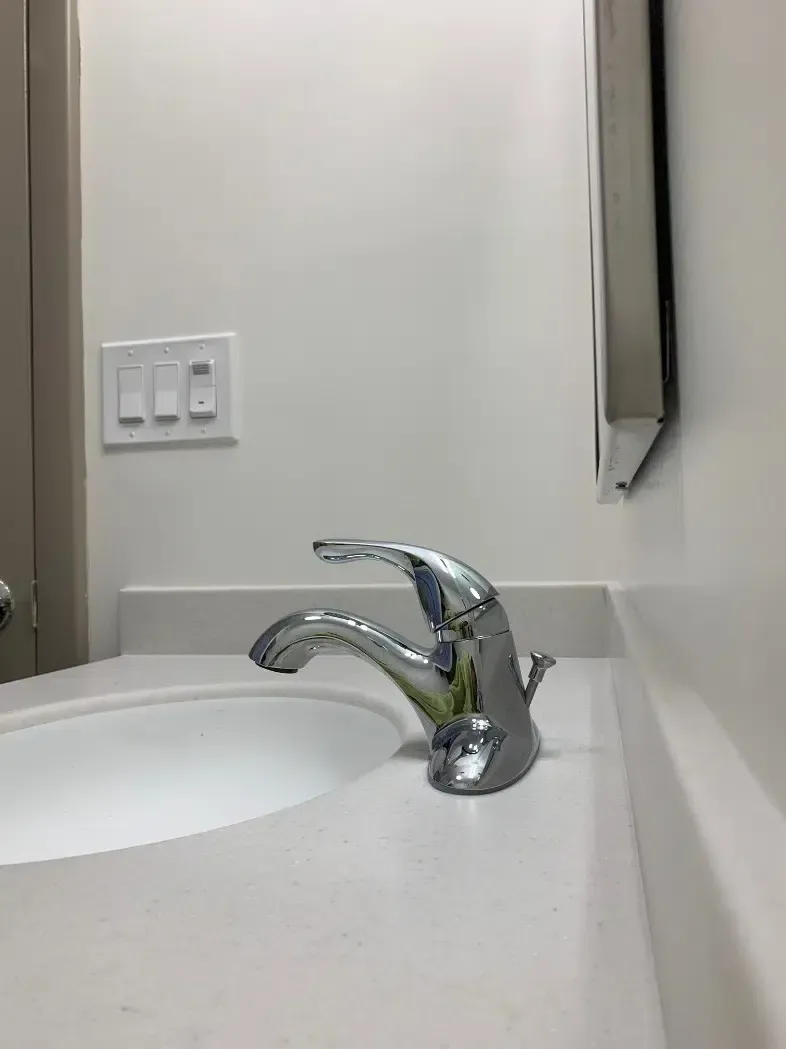 Bathroom sink with chrome faucet, white countertop, and wall mirror near light switches.
