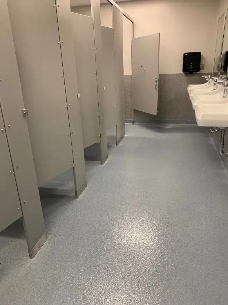 Public restroom with gray stalls, white sinks, and blue speckled floor