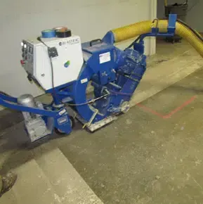 Blue industrial floor machine with a yellow hose in a concrete basement or utility area