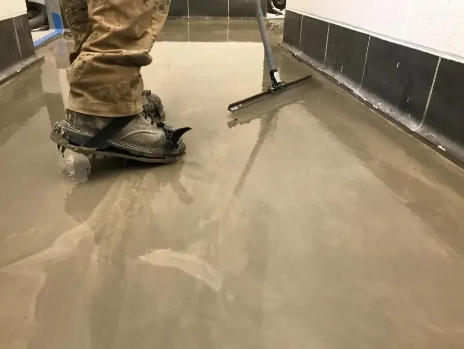 Worker smoothing wet concrete floor with a trowel in a tiled hallway