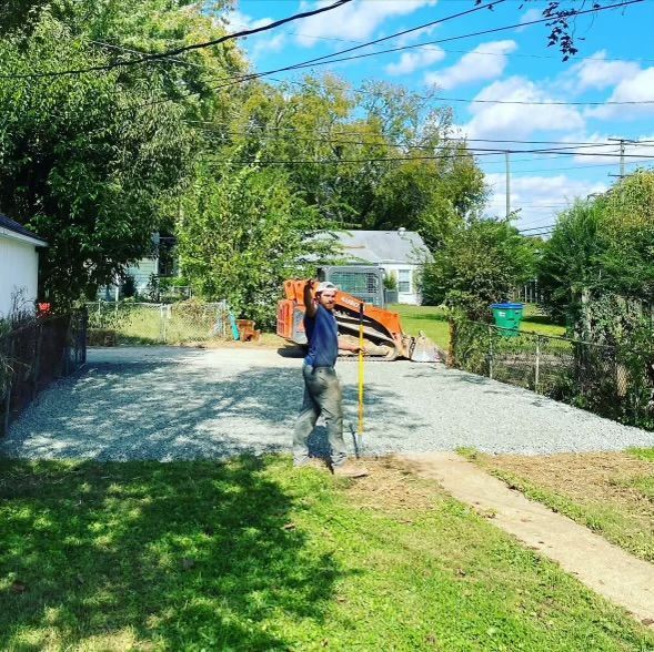 A man is standing in front of a gravel driveway next to a house.