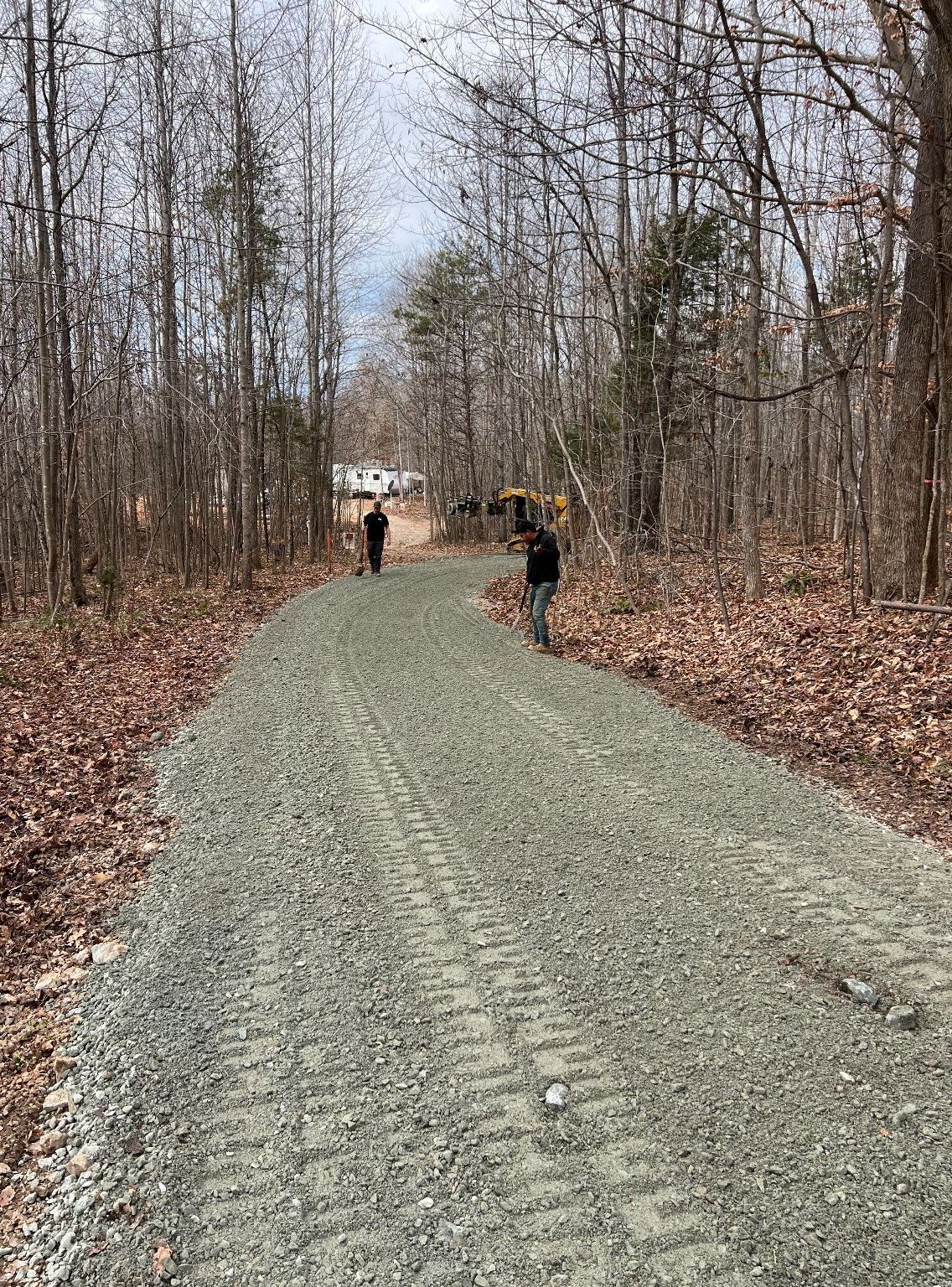 Two people are walking down a gravel road in the woods.