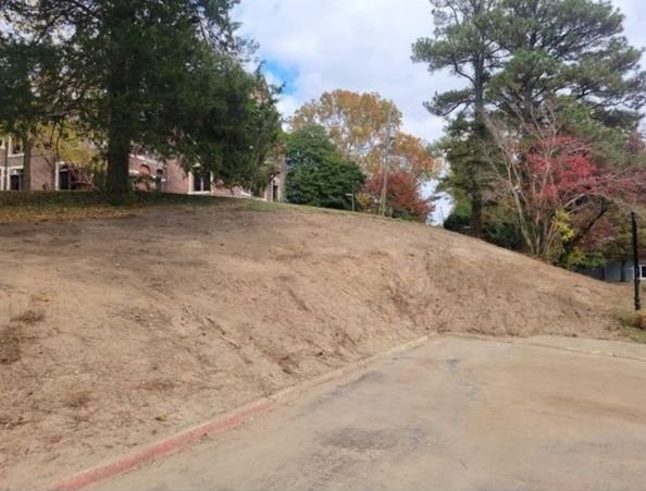 A dirt hill with trees in the background and a basketball court in the foreground.