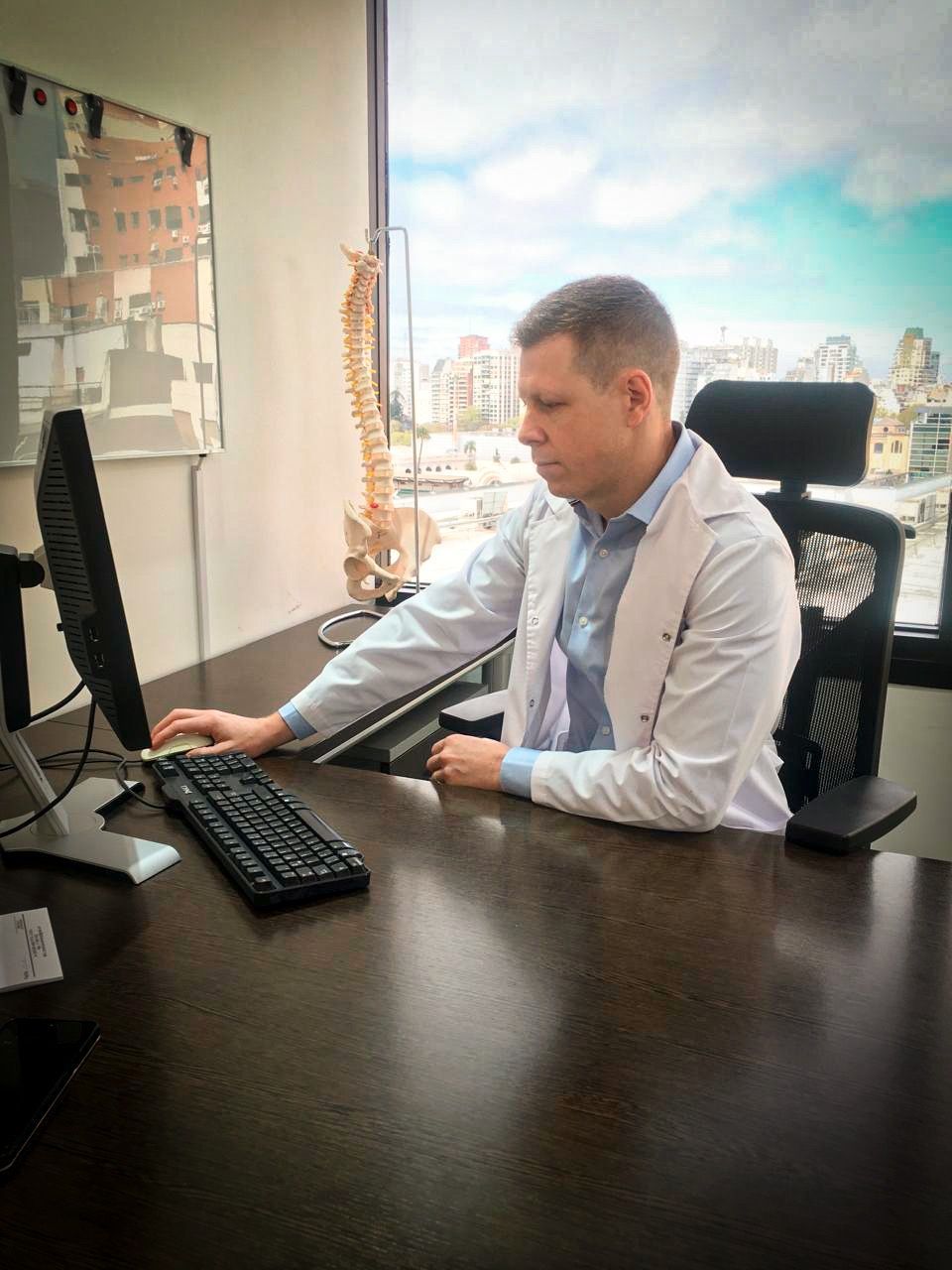 Doctor escribiendo en el teclado en el escritorio; estetoscopio, gafas y rayos X presentes.