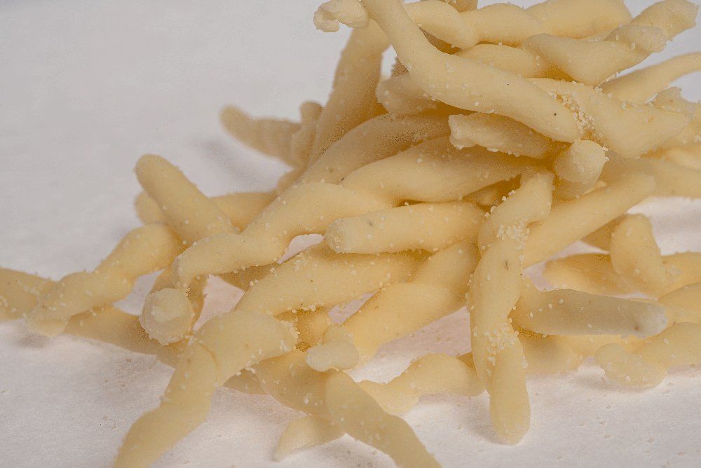 Mucchio di pasta fresca strozzapreti, di colore giallo paglierino, su una superficie bianca.