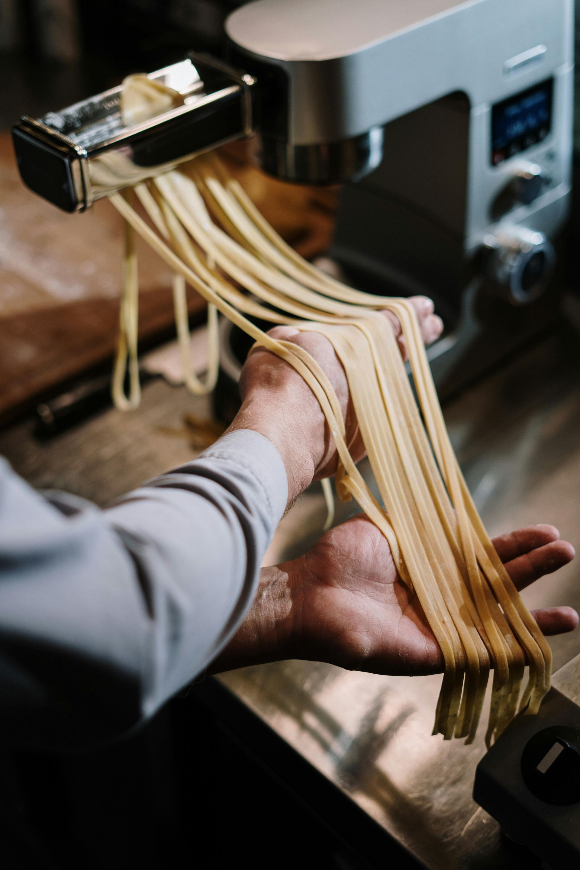 Mani che tengono in mano fili di pasta fresca tirati dalla macchina per la pasta.