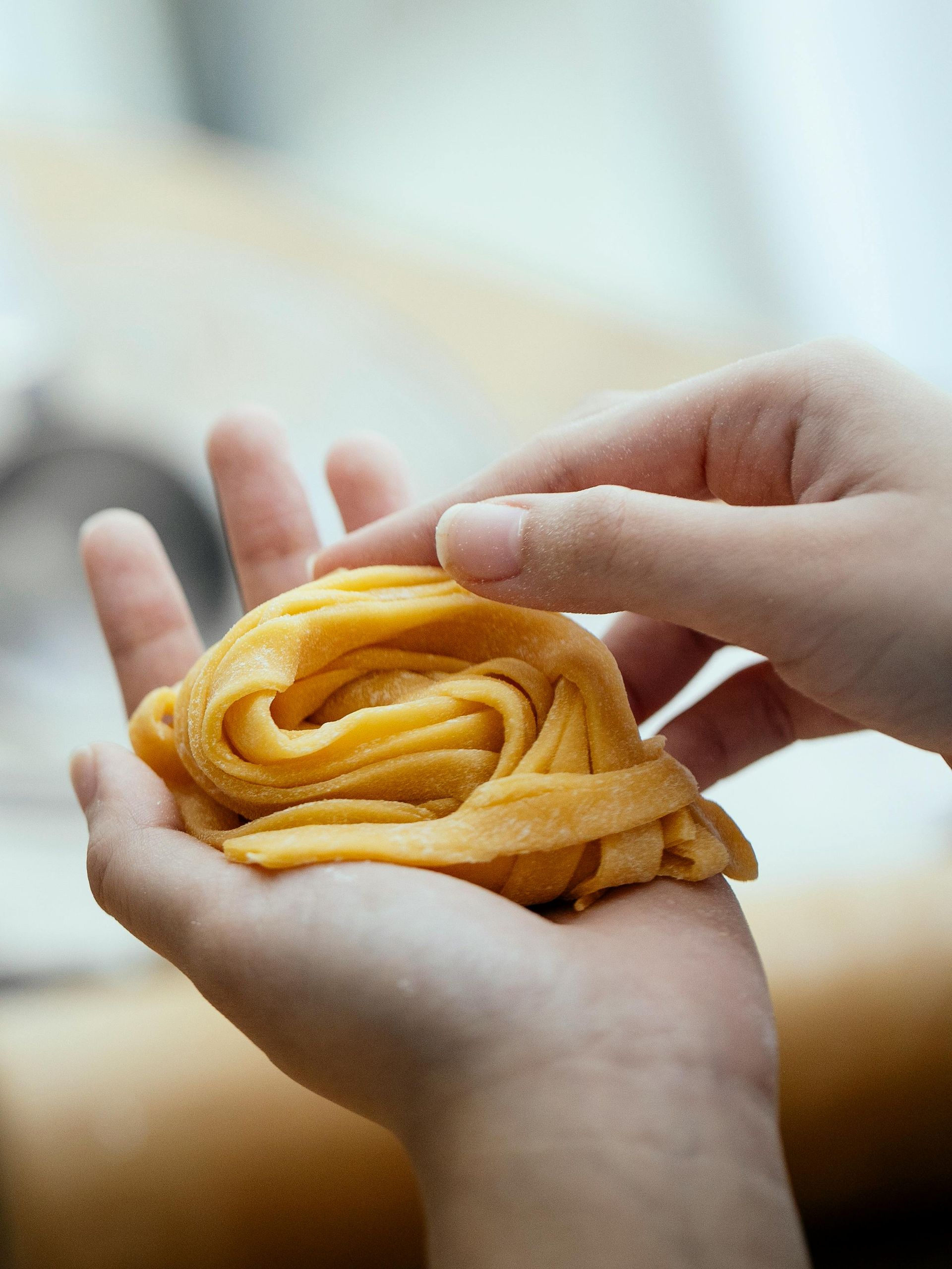 Mani che tengono un nido di pasta gialla, preparandolo per la cottura.