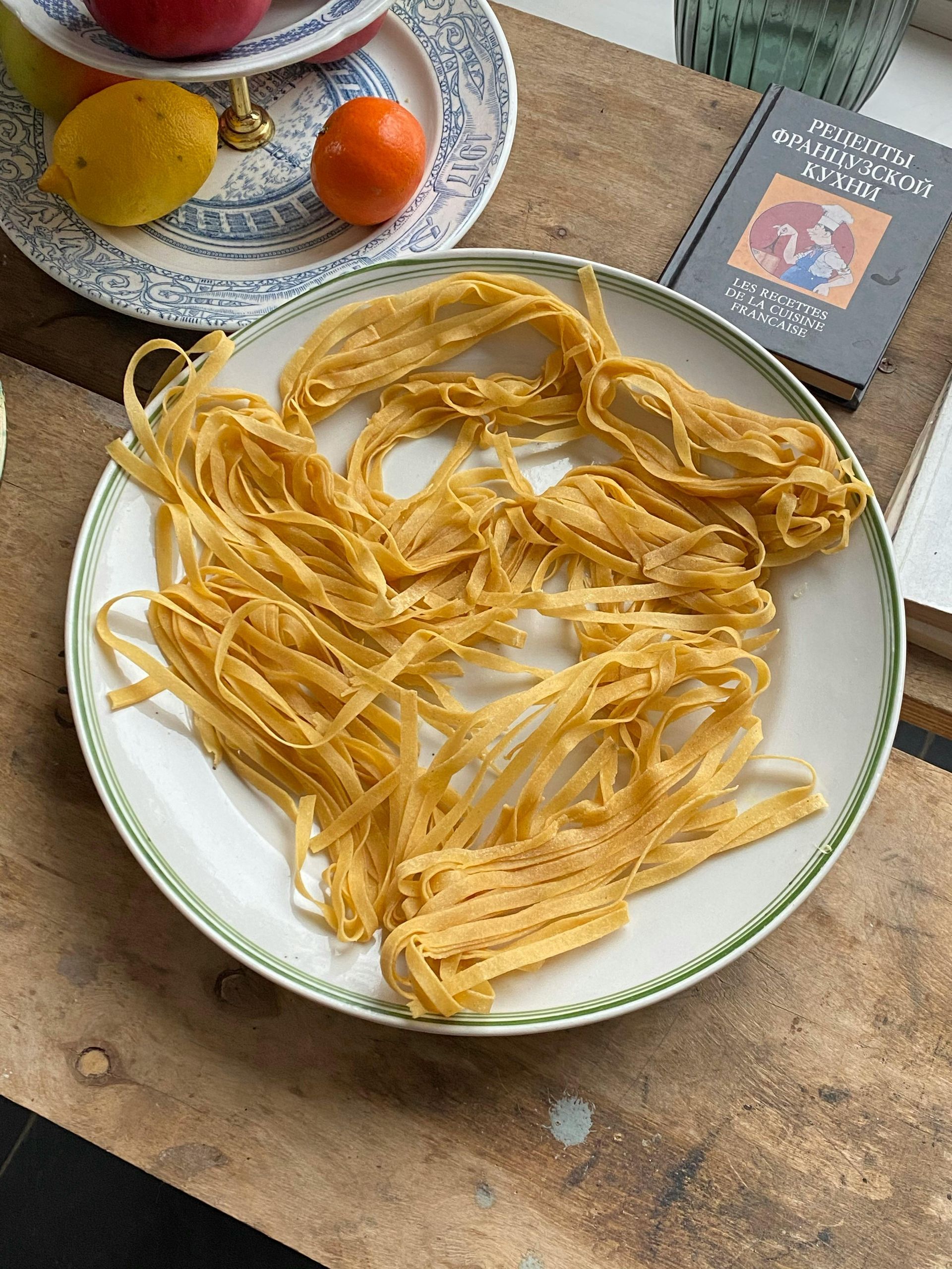 Pasta su un piatto, frutta su un piatto e un libro su un tavolo di legno.