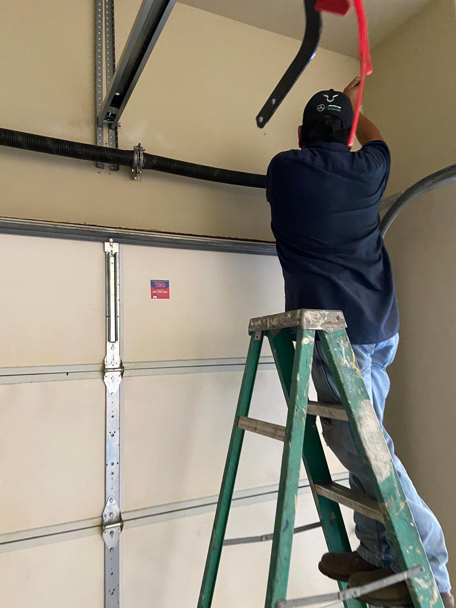 A person stands on a ladder working on the overhead components of a closed garage door.