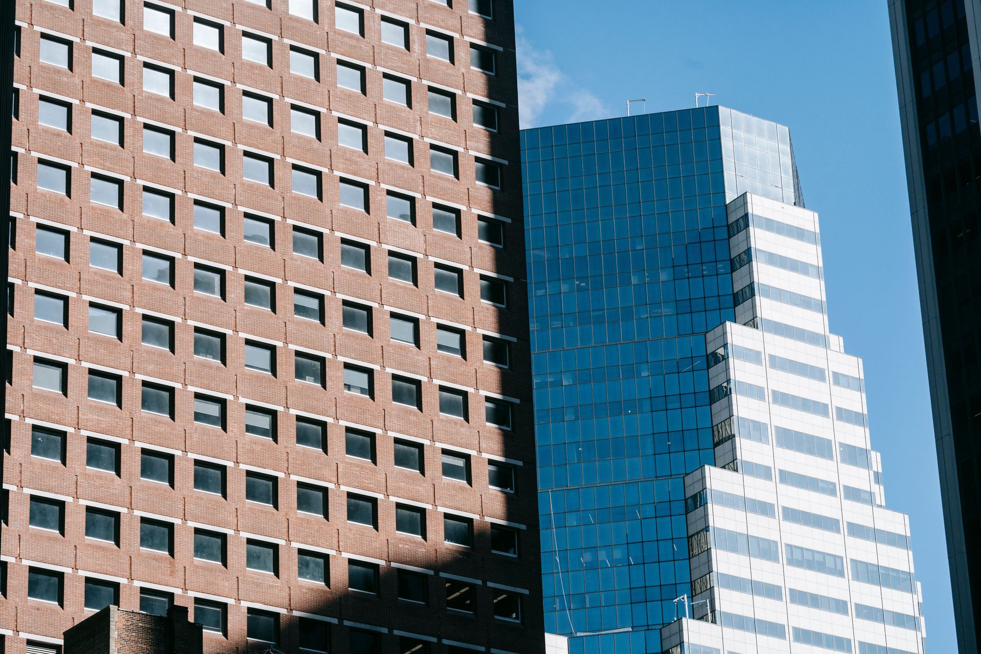 Tall office buildings with a brown brick facade, blue glass tower, and white stepped skyscraper against a clear sky