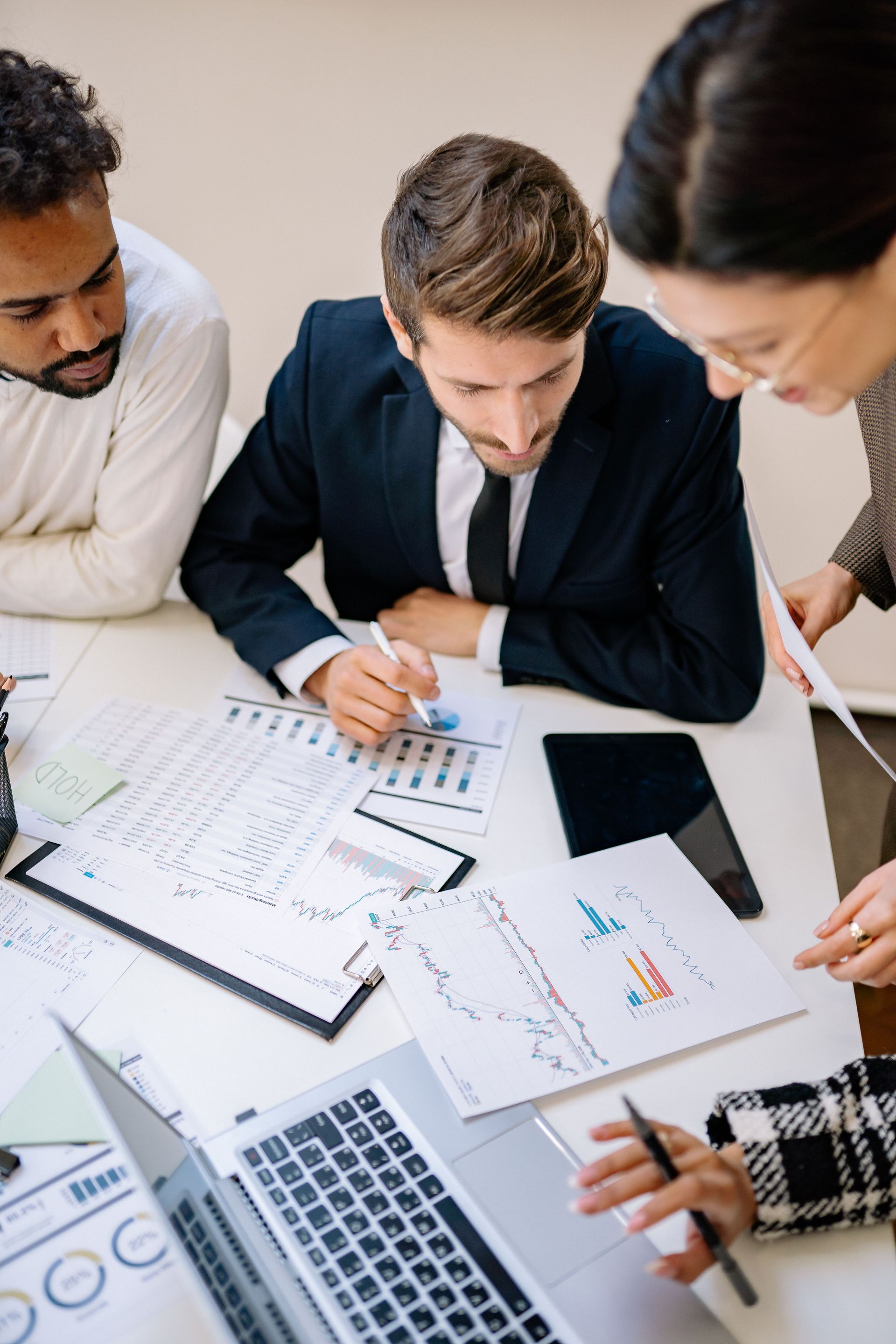 Team collaborating around a desk with charts, laptop, and documents during a business meeting