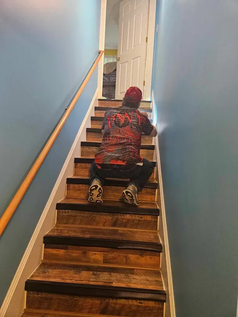 Child crawling up wooden stairs in a blue-walled hallway toward an open door