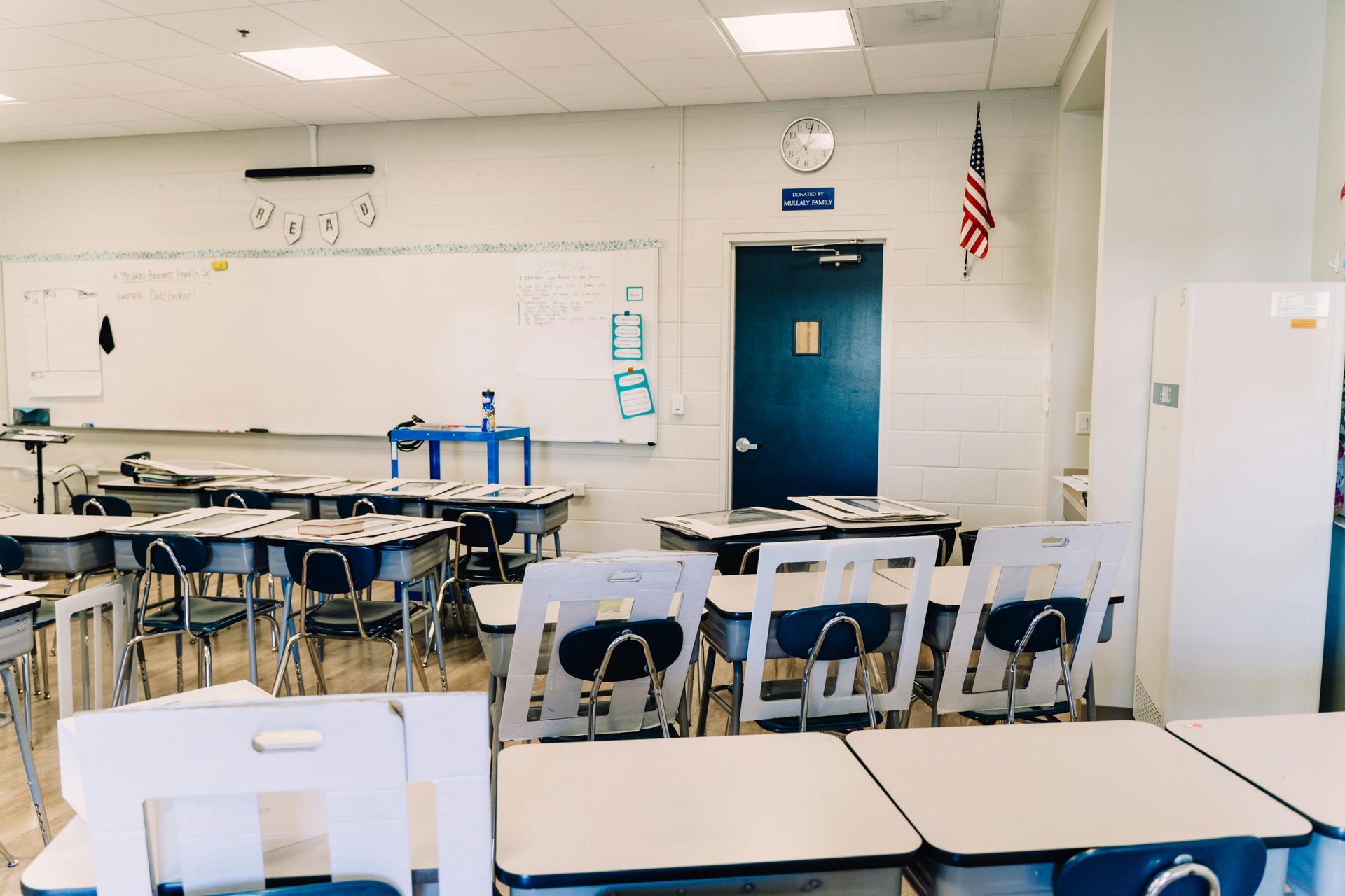 Empty classroom with desks, whiteboard, blue door, and an American flag on the wall