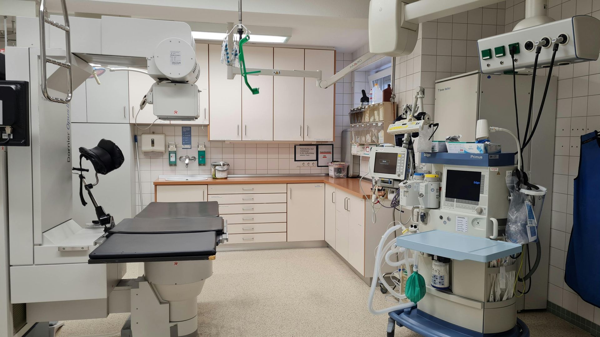 Empty veterinary exam room with x-ray table, cabinets, and medical equipment on the walls and counter