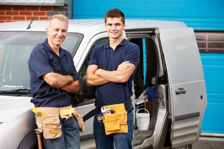 Two workers in tool belts standing beside a silver van with the side door open