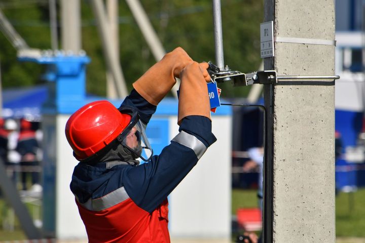 Worker in red hard hat fastening a cable to a concrete utility pole outdoors