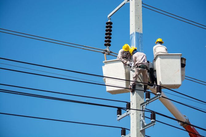 Utility workers in yellow helmets repairing power lines from bucket trucks on a utility pole