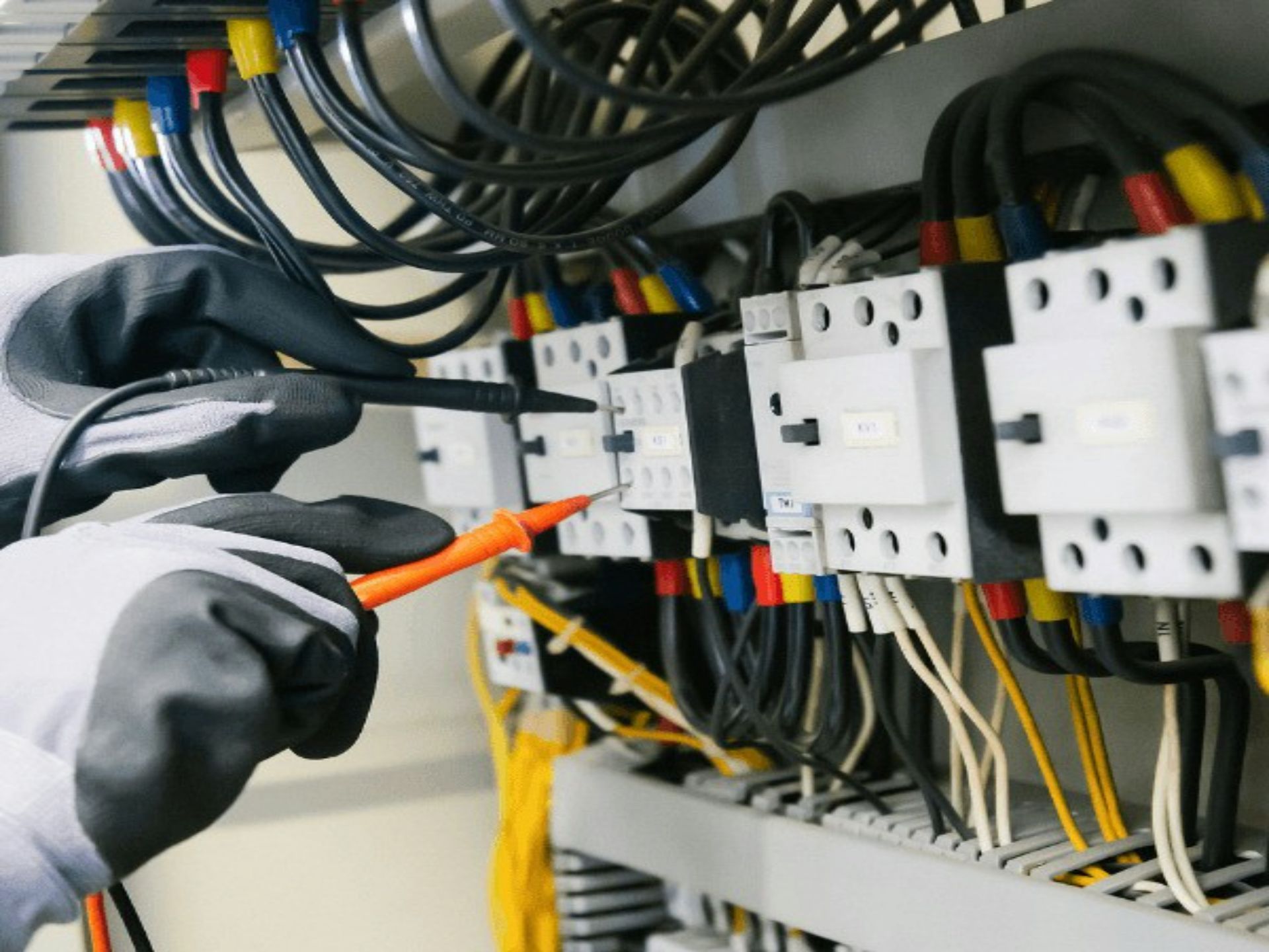Gloved hands wiring an electrical control panel with colored cables and circuit breakers