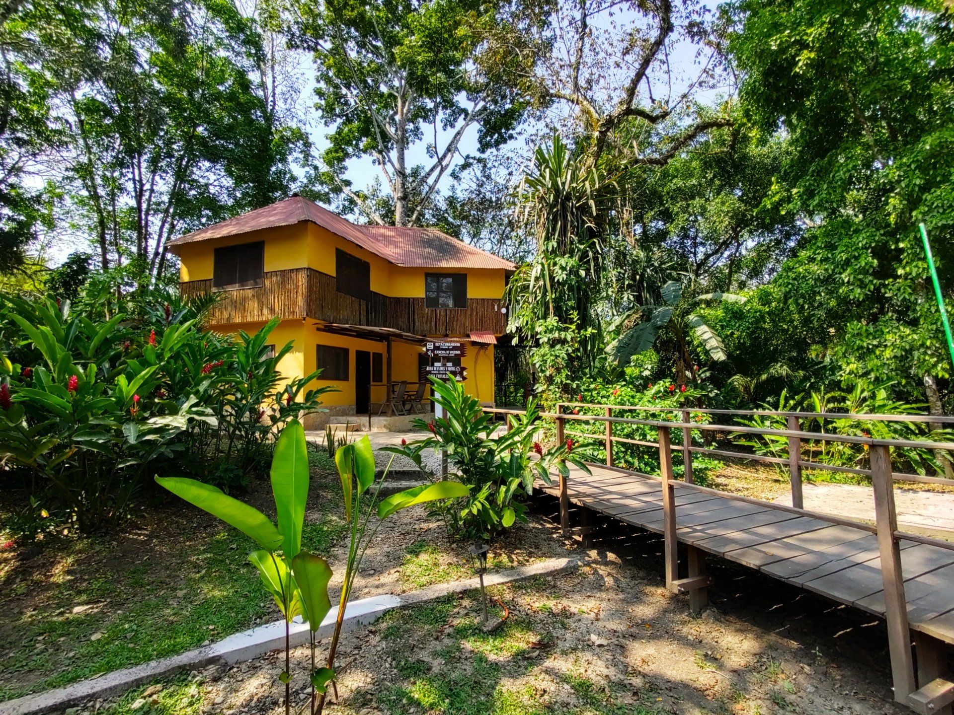 Una casa amarilla está rodeada de árboles y un puente de madera.