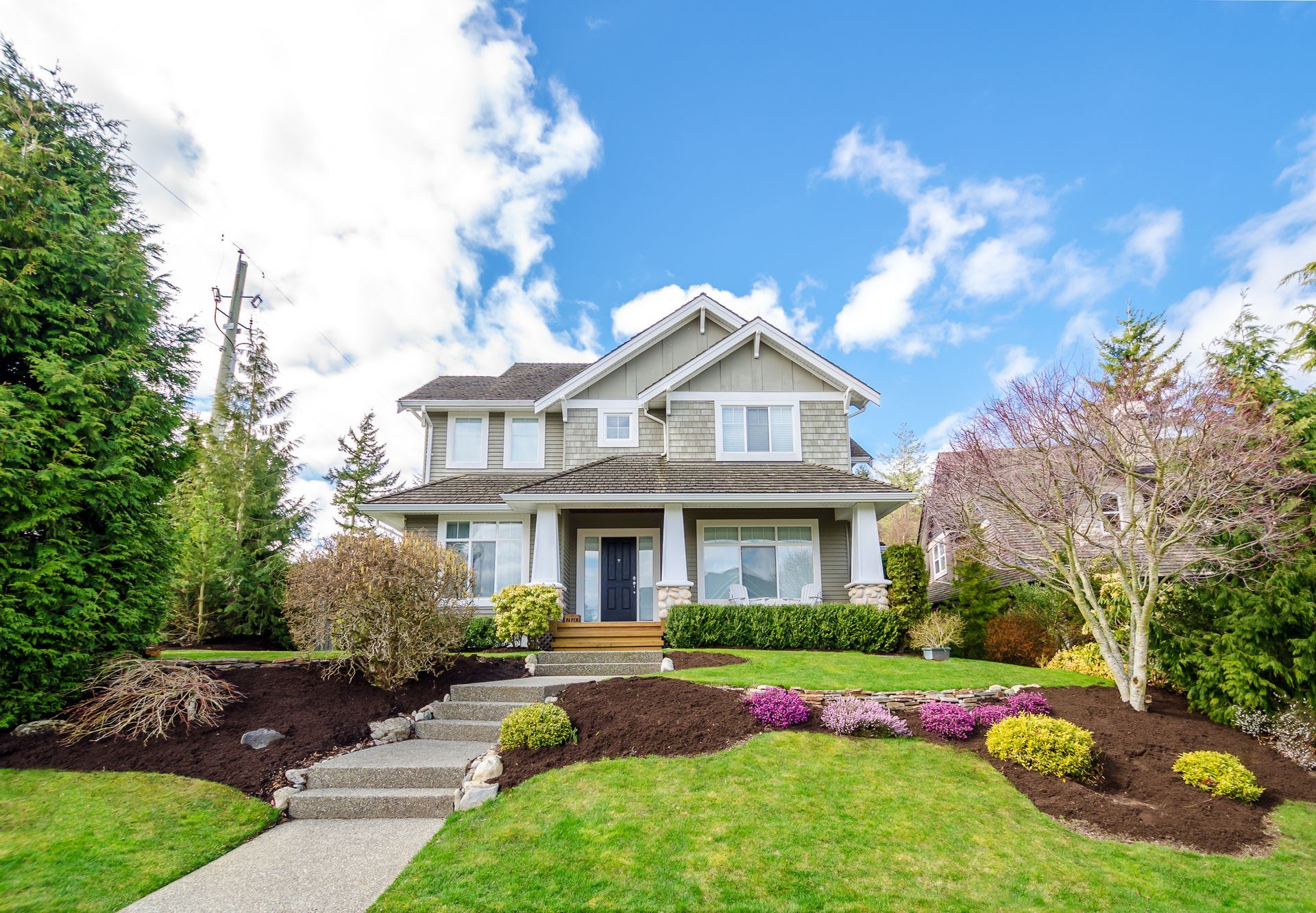 Two-story house a landscaped yard with green grass, bushes, and a blue sky.