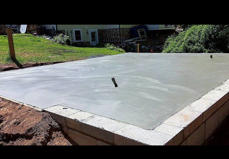 Newly poured concrete slab in the front yard of a house. The slab will hold a small garage or shed.