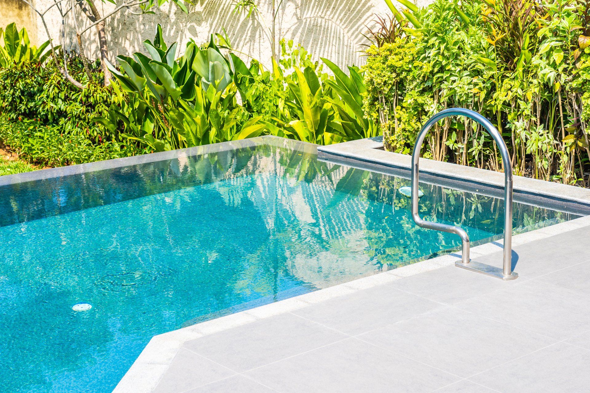 Closeup picture of a backyard pool surrounded by plants. The pool is also bordered by a stamped concrete pool deck in Peterborough.