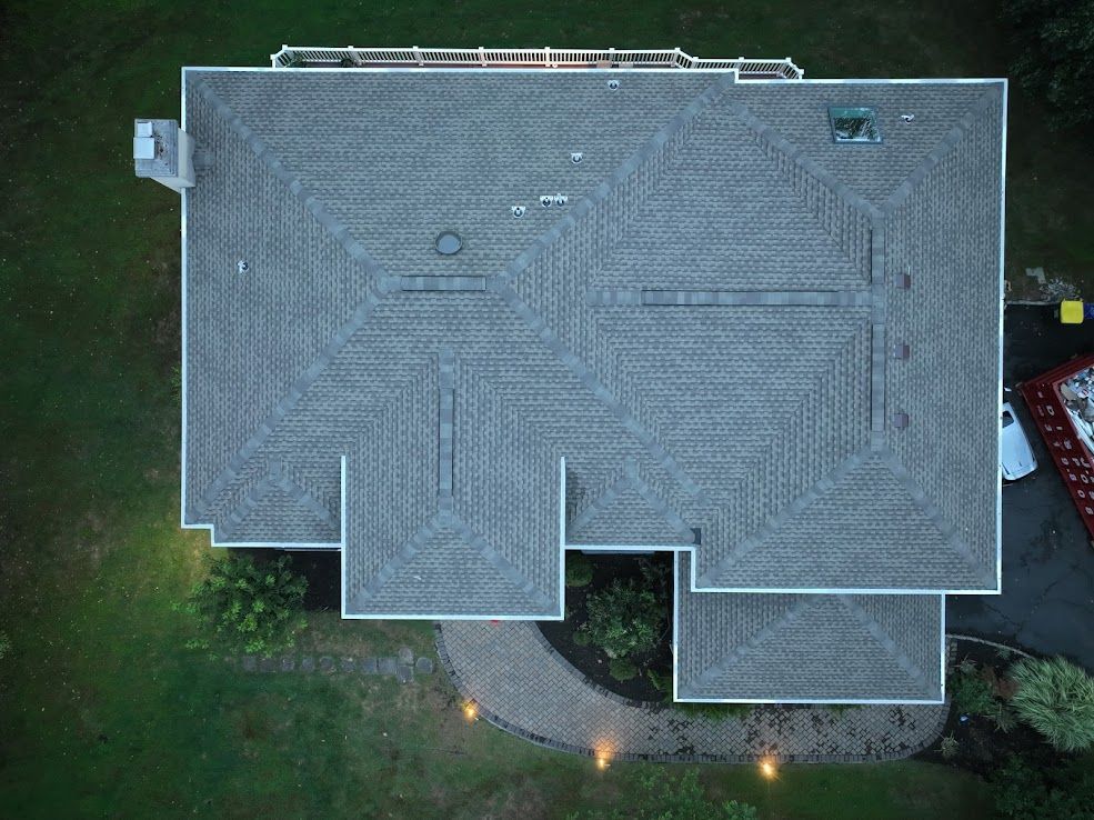 Overhead view of a house with a gray shingled roof, set in a green yard with a stone path.