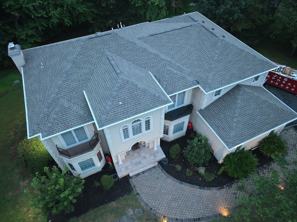 Aerial view of a two-story beige house with a gray roof and a circular driveway.