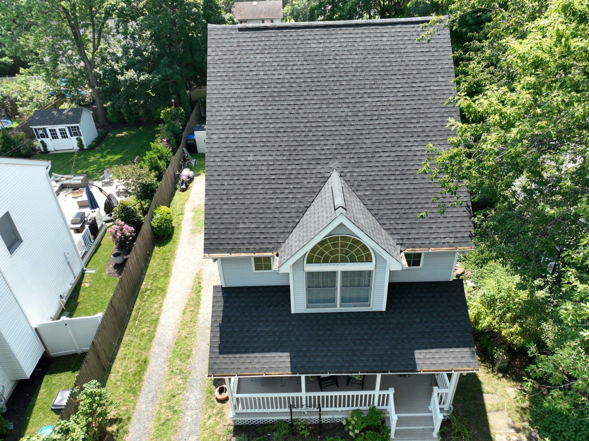 Aerial view of a gray house with a dark roof and a small white porch. Surrounded by green trees and grass.