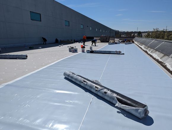Roofing work in progress; rolls of light blue material on a rooftop, with workers visible.