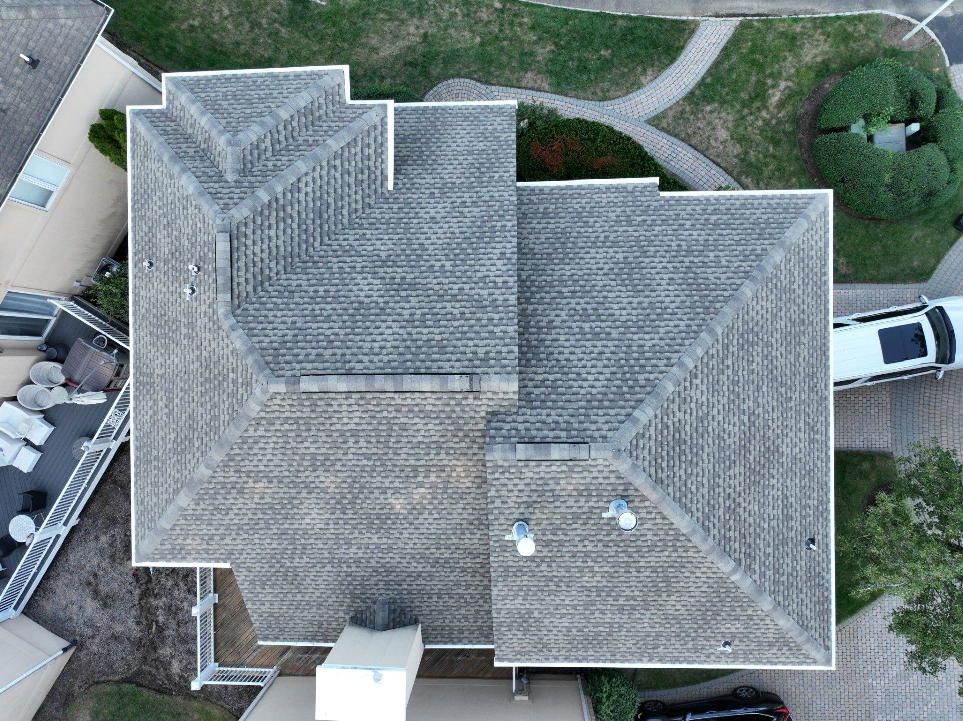 Overhead view of a gray roof with vents, white trim, and a car parked in a driveway.