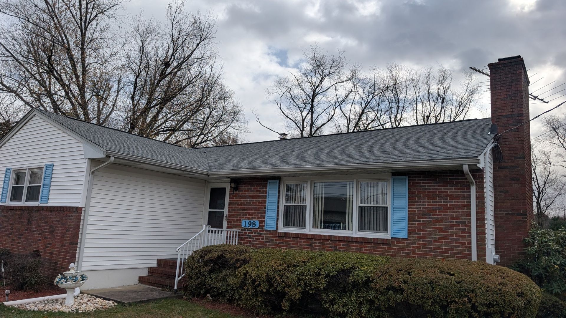House with brick and white siding, blue shutters, and a chimney under a cloudy sky.