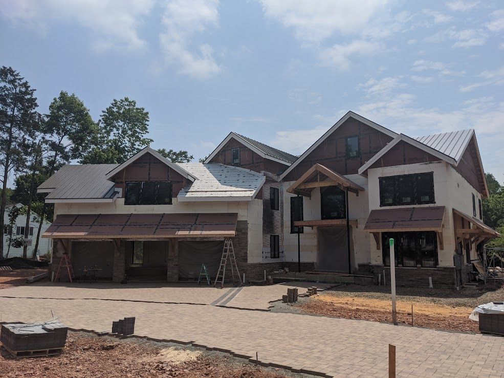 House under construction with stone accents, tan siding, and light grey metal roof.