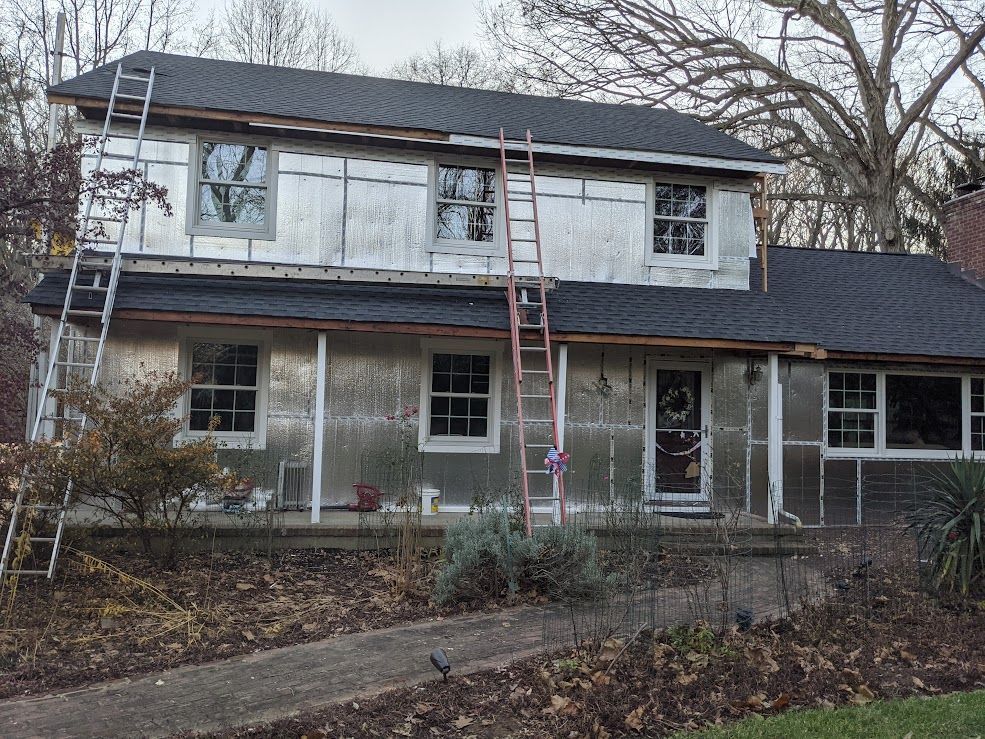 House under renovation, covered in silver insulation. Ladders lean against the structure.