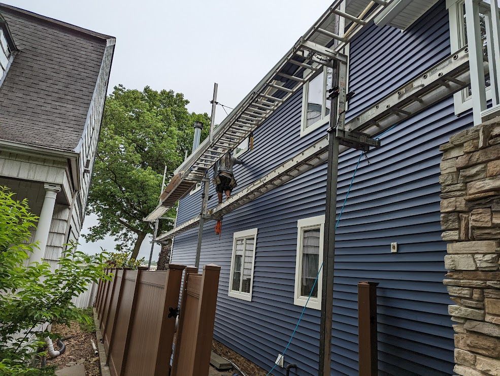 House exterior with blue siding, scaffolding, ladder, and a worker.