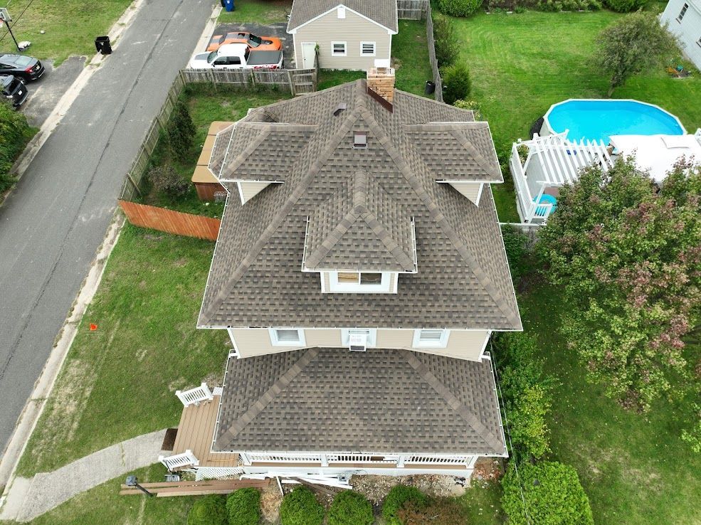 Overhead view of a multi-story house with a brown roof, surrounded by green grass and a small above-ground pool.